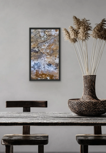 Im Hintergrund hängt ein buntes, vollflächiges Steinbild an einer hellgrauen Wand, vor der ein Tisch mit zwei Stühlen und eine Vase stehen.