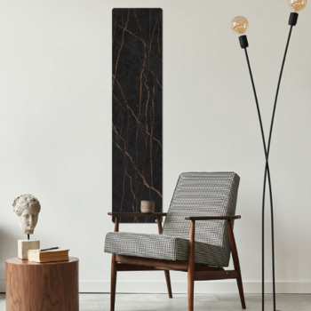 Anthrazitfarbene, marmorierte Infrarotheizung hängt an einer weißen Wand, vor der ein Sessel, eine Stehlampe und ein Beistelltisch mit Deko stehen.