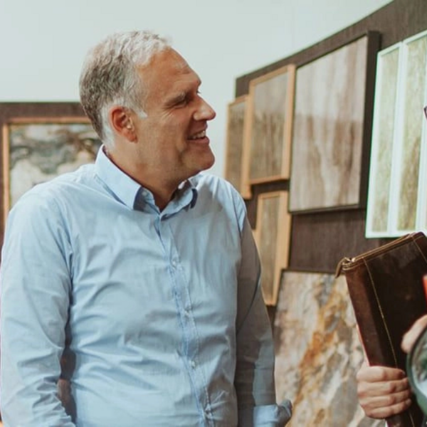 Zwei Personen werden von einem Steinbildhändler beraten und im Hintergrund hängen diverse Steinbilder.