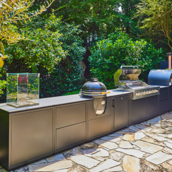 Große Außenküche steht vor grünen Büschen in einem Garten.