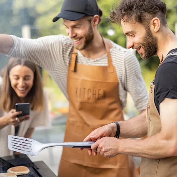 Drei junge Erwachsene kochen fröhlich draußen in einem Garten mit Außenküche.