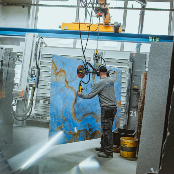 Arbeiter bewegt ein großes Steinbild mit einer Hebevorrichtung in einer Werkhalle.