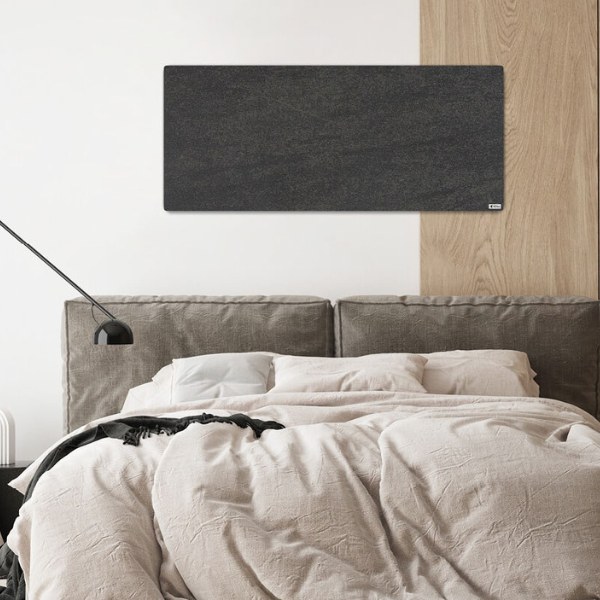 Anthrazitfarbene Infrarotheizung hängt in einem modernen Schlafzimmer über einem gemütlichen Bett.